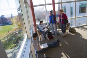 Students studying in a building on campus with sunlight shining through windows.