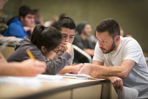 Graduate student aiding students during professor's lecture.