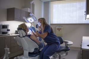 A patient reclines in a dentist chair while a dentist examines them.