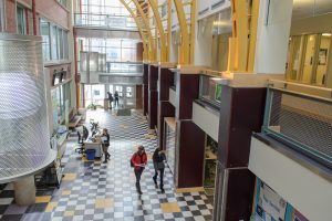 Students walk in a large hallway with high, arched ceilings and a checkered tile floor.