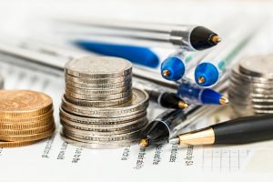 Stacks of coins and pens on top of paperwork.