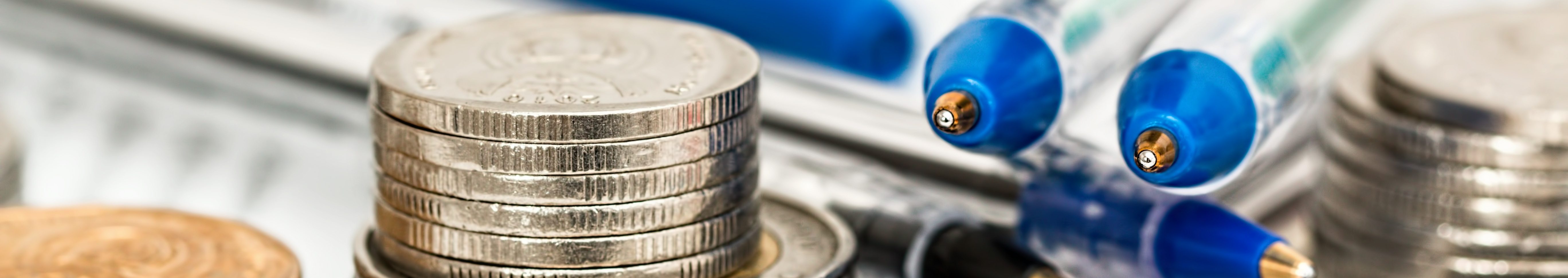 Stacks of coins and pens on top of paperwork.